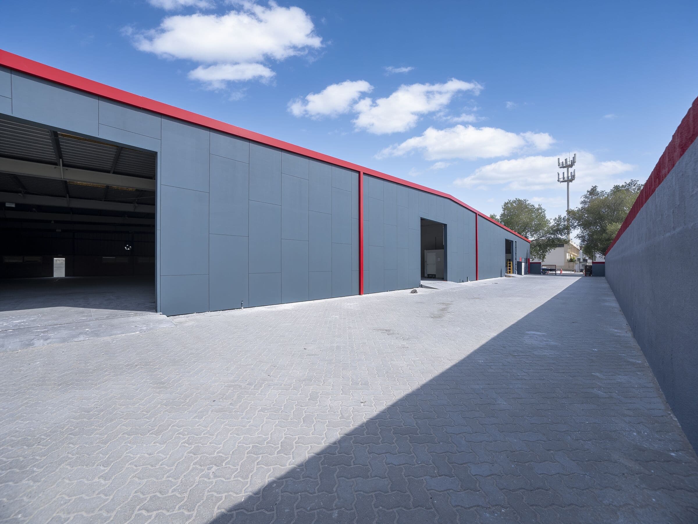 Grey warehouse units with red trim and open loading bays along the paved lane at Motor Garten